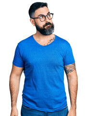 Hispanic man with beard wearing casual t shirt and glasses smiling looking to the side and staring away thinking.