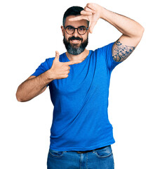Hispanic man with beard wearing casual t shirt and glasses smiling making frame with hands and fingers with happy face. creativity and photography concept.