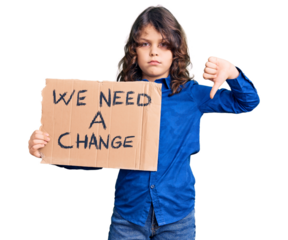 Cute hispanic child with long hair holding we need a change banner with angry face, negative sign showing dislike with thumbs down, rejection concept
