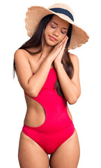Young beautiful latin girl wearing swimwear and summer hat sleeping tired dreaming and posing with hands together while smiling with closed eyes.