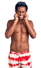 Fototapeta premium African handsome man wearing swimsuit and sunglasses covering ears with fingers with annoyed expression for the noise of loud music. deaf concept.