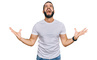 Young man with beard wearing casual white t shirt crazy and mad shouting and yelling with aggressive expression and arms raised. frustration concept.