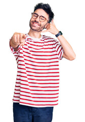 Fototapeta premium Young hispanic man wearing casual clothes smiling doing talking on the telephone gesture and pointing to you. call me.