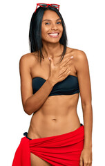 Fototapeta premium Young african american woman wearing bikini cheerful with a smile of face pointing with hand and finger up to the side with happy and natural expression on face