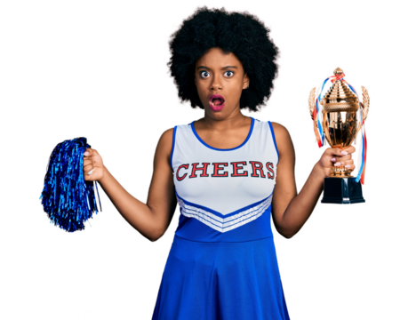 Young african american woman wearing cheerleader uniform holding pompom and trophy in shock face, looking skeptical and sarcastic, surprised with open mouth