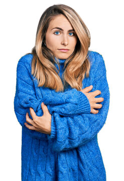 Young blonde woman wearing casual sweater shaking and freezing for winter cold with sad and shock expression on face