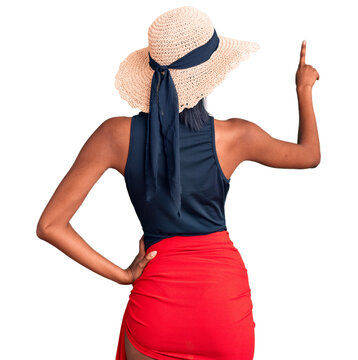 Young african american woman wearing swimsuit and summer hat posing backwards pointing ahead with finger hand