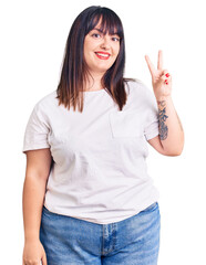 Young plus size woman wearing casual clothes smiling looking to the camera showing fingers doing...