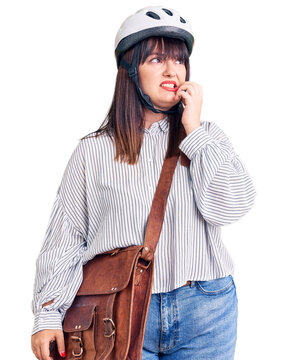 Young plus size woman wearing bike helmet and leather bag looking stressed and nervous with hands on mouth biting nails. anxiety problem.