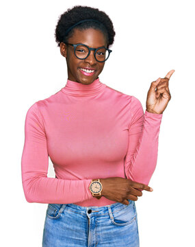 Young african american girl wearing casual clothes and glasses with a big smile on face, pointing with hand and finger to the side looking at the camera.