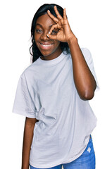 Young african american woman wearing casual white t shirt doing ok gesture with hand smiling, eye looking through fingers with happy face.