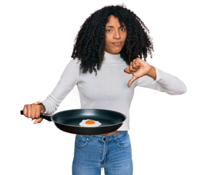 Young african american girl holding skillet with fried egg with angry face, negative sign showing dislike with thumbs down, rejection concept