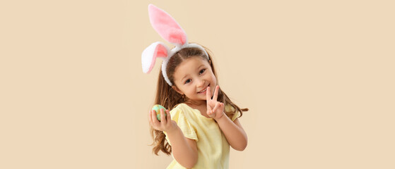 Little girl with bunny ears and Easter egg on beige background