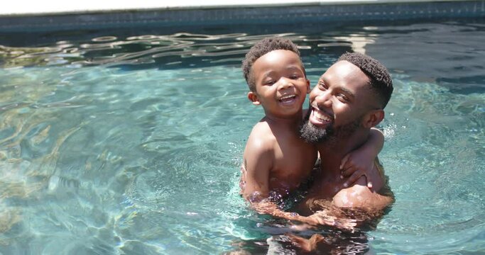 Portrait of happy african american father and son playing at pool, in slow motion