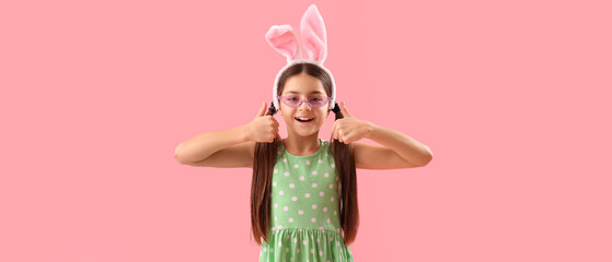 Cute little girl with bunny ears showing thumb-up on pink background