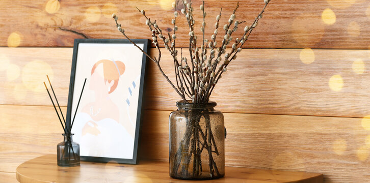 Vase with willow branches and picture near wooden wall in room