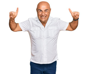 Mature middle east man with mustache wearing casual white shirt smiling amazed and surprised and pointing up with fingers and raised arms.