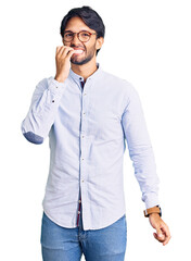 Handsome hispanic man wearing business shirt and glasses looking stressed and nervous with hands on mouth biting nails. anxiety problem.