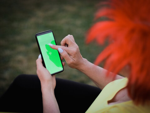 Caucasian woman wearing a Belgian flag wig holding a smartphone with a green screen pointing her finger at it.