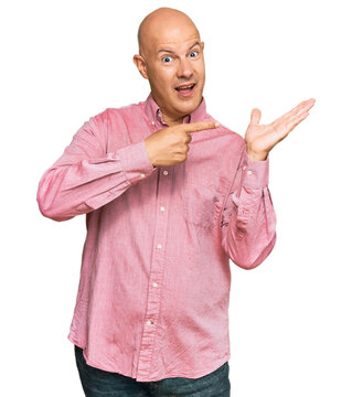 Middle age bald man wearing casual clothes amazed and smiling to the camera while presenting with hand and pointing with finger.