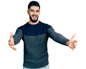 Young arab man with beard wearing casual sweater looking at the camera smiling with open arms for hug. cheerful expression embracing happiness.