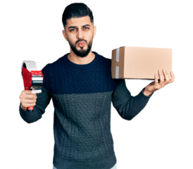 Young arab man with beard holding packing tape and cardboard box looking at the camera blowing a kiss being lovely and sexy. love expression.