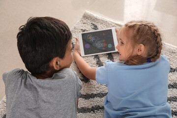 Little girl and her brother watching cartoons on tablet computer on floor, back view