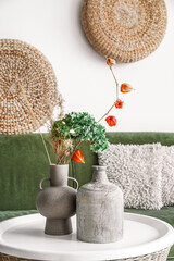 Vases with flowers on rattan table in living room