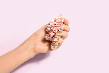 Female hand with stylish silk scrunchies on pink background