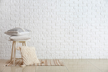 Stylish pillows on stool against light brick wall
