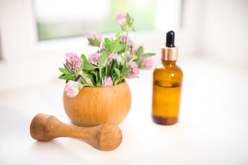 Cosmetic bottle made of dark glass with a dispenser on a white background with fresh clover. Production of essential oil for cosmetology