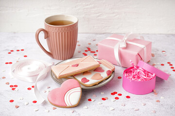 Plate with tasty cookies, cup of tea and gift box on light background. Valentine's Day celebration
