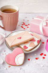 Plate with tasty cookies, cup of tea and gift box on light background. Valentine's Day celebration