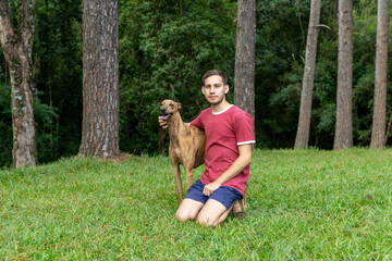Naklejka na ściany i meble hombre joven, caucasico, con un perro galgo, disfrutando al aire libre.