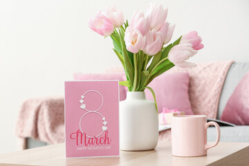 Vase with tulips, cup and greeting card for Women's Day on table in living room