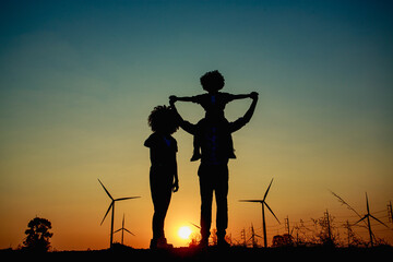 Silhouettes of Happy family father, mother and child daughter sits on the shoulders of his father with windmills for electricity generation at sunrise by producing sustainable energy  © AU USAnakul