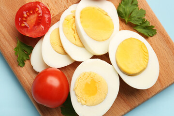 Board with delicious boiled eggs, tomatoes and parsley on blue background