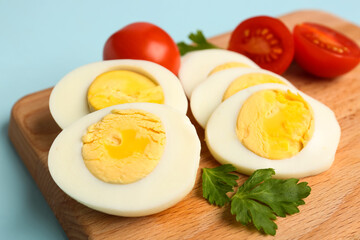 Board with delicious boiled eggs, tomatoes and parsley on blue background