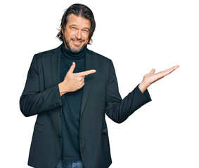 Middle age handsome man wearing business clothes amazed and smiling to the camera while presenting with hand and pointing with finger.