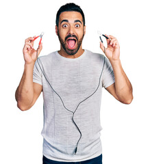 Young hispanic man with beard holding battery clamps celebrating crazy and amazed for success with...