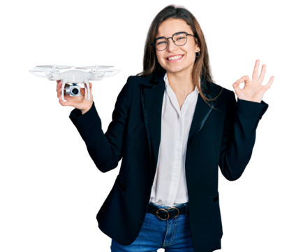 Young caucasian girl wearing business style holding drone doing ok sign with fingers, smiling friendly gesturing excellent symbol