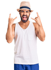Young hispanic man wearing casual summer hat shouting with crazy expression doing rock symbol with hands up. music star. heavy concept.