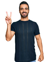 Fototapeta premium Young hispanic man wearing casual clothes smiling with happy face winking at the camera doing victory sign. number two.