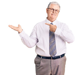 Senior grey-haired man wearing business clothes amazed and smiling to the camera while presenting with hand and pointing with finger.