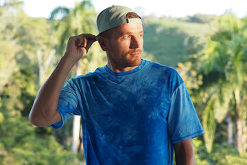 Portrait confident man wears blue t-shirt and green baseball hat in tropical environment  .
