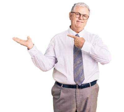 Senior grey-haired man wearing business clothes amazed and smiling to the camera while presenting with hand and pointing with finger.