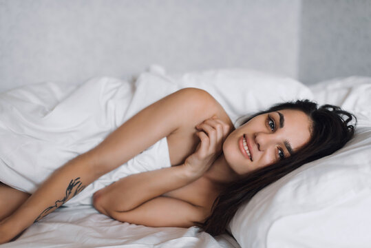 sexy happy nude beautiful brunette girl smiling in bed under a blanket in bedroom