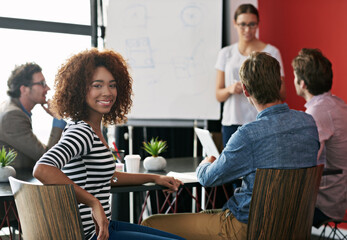 Success motivates my team. Portrait of a young office worker in a meeting with colleagues in the background.