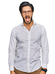 Young hispanic man wearing business shirt and glasses sticking tongue out happy with funny expression. emotion concept.