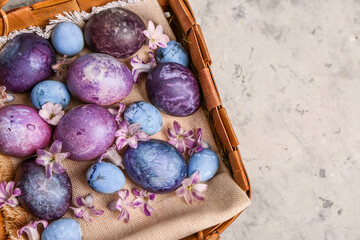 Basket with painted Easter eggs and violet flowers on grey grunge background